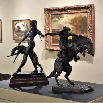 Two sculptures on a pedestal in front of a wall of paintings