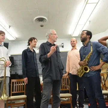 A man talks with a group of college students holding musical instruments