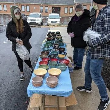 Two volunteers helping a person select their bowl outside during our Potter's Bowl event during 2020