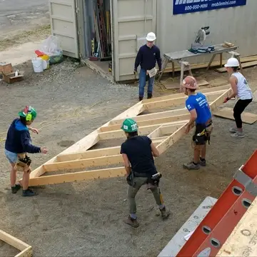 Four young adults lifting a wooden wall frame on a construction site