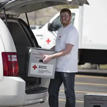 Man loading blood transportation container into Red Cross van