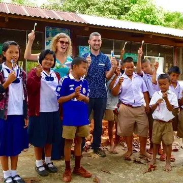 American volunteers smiling with Thai students, holding toothbrushes