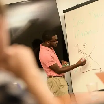 an african american male  draws a graph on a white board while students look on
