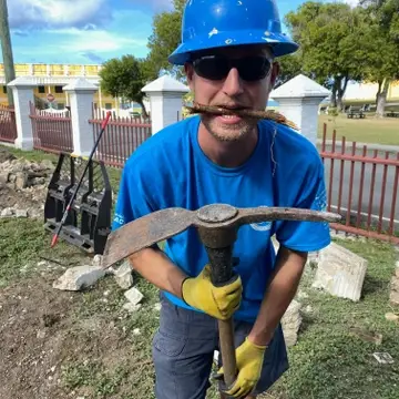 National service member, in a blue shirt holding a pick-mattock digging tool.