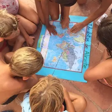 A group of children gather around a map that says Idealista on it.