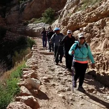 A group hiking down a desert trail. Everyone in the group holds a cane.