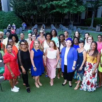 A group of women at an outdoor event space who are dressed up and gathered together for a group photo.