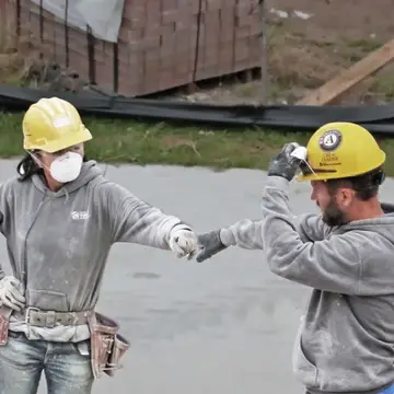 Man and woman in hard hats covered in dust bump fists
