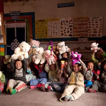 group of toddler aged children smile and hold up plush toys