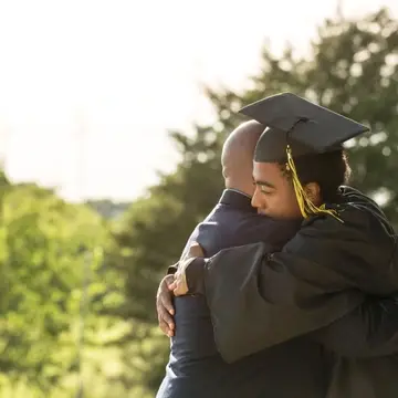 Young man in graduation cap hugs older man
