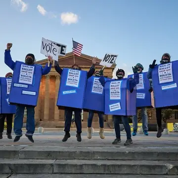 People dressed in mail-in ballot boxes or mailboxes jump and dance for democracy in Philadelphia.