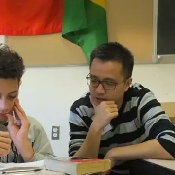 Middle school student in a hoodie and adult tutor with glasses look at a problem together.