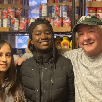 Three partners of Good Shepherd Food Bank of Maine in a food pantry with shelves in the background.