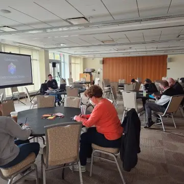 Attendees sit at round tables in a bright, windowed room with a presentation screen displaying "SONIC CONNECTIONS."