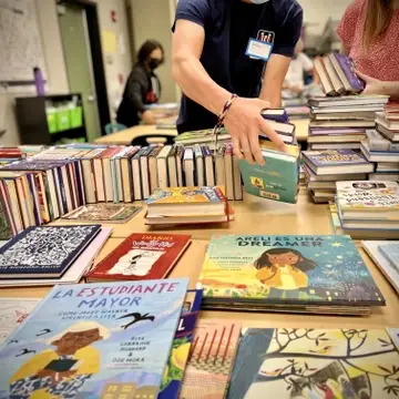 a bunch of new books on a table getting prepared by volunteers for the library.