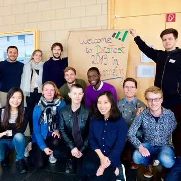 Group of students around a sign that reads "Welcome to DataFest 2019 in Mannheim."
