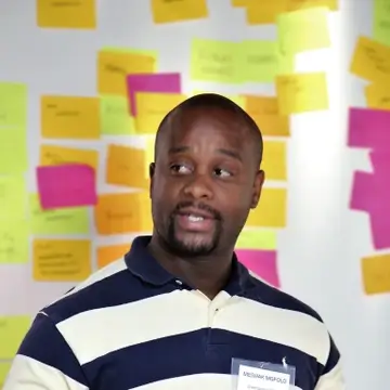 A man speaks in front of a wall of multicoloured post-its
