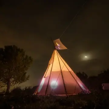 Tipi lit from the inside against a night sky with moon.