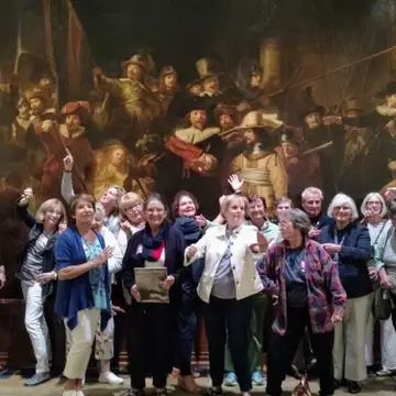 A group of older adults posing in front of a copy of "The Night Watch"
