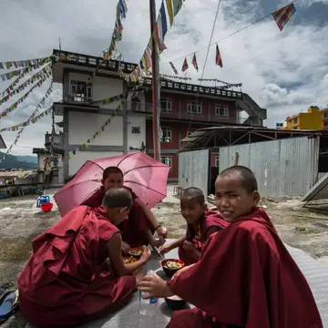 Group of young Buddhist nuns sit outside with bowls of food and prayer flags hang above