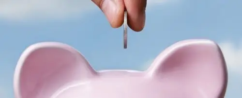 Close up of a coin going in to a piggy bank.