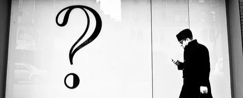 A man walks behind a question mark printed on a store window.