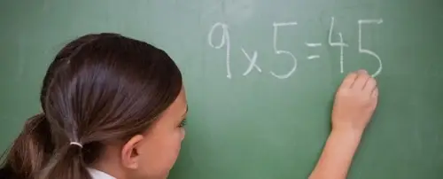 A little girl writes a math equation on a chalkboard.