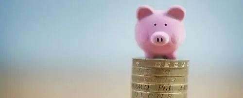 A piggy bank at the top of a pile of coins.