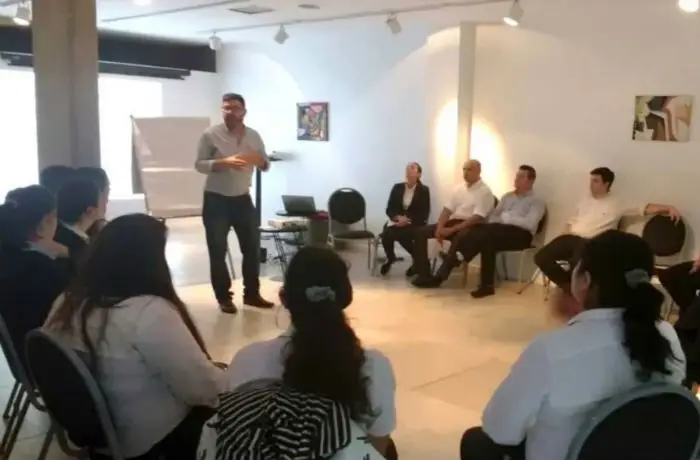 A group of people sitting in a circle, with someone speaking to them in the middle.