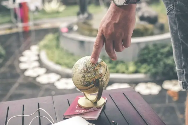 A man's hand touches a small globe.