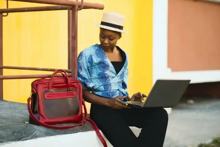 A young woman with her laptop open looks down at her bag.