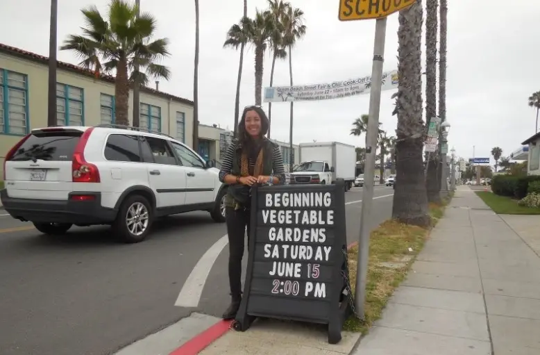 Destiny Rivera posa ao lado de anúncio sobre hortas de vegetais