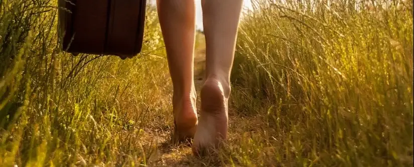 A person holding a bag and walking barefoot in a field.