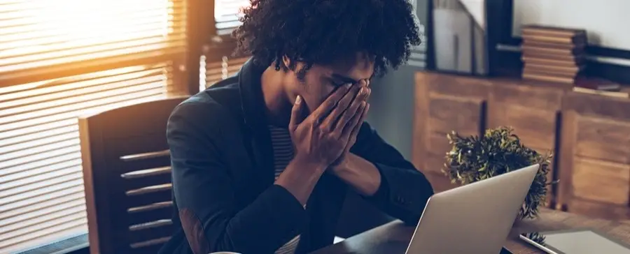 A tired man sighing over a laptop.