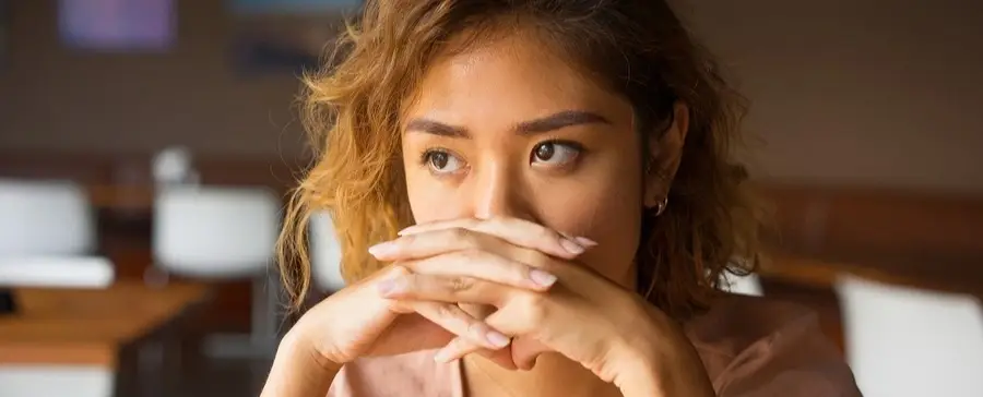 A woman with her hands folded in front of her face.