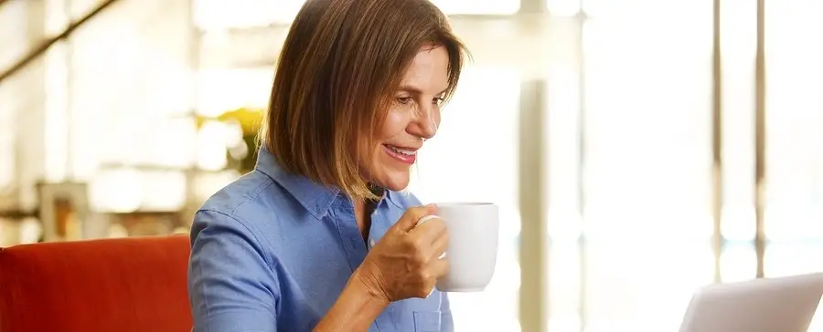 A woman sits at a laptop drinking coffee.