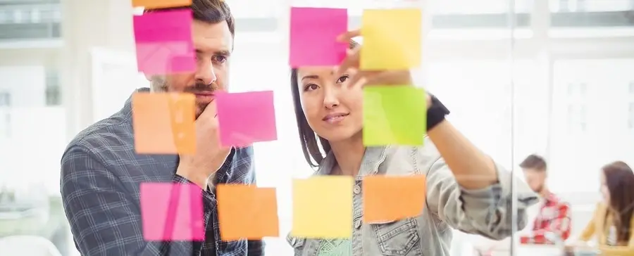Two people looking at post its, stuck on a glass.