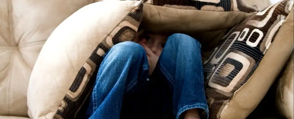 A little boy hiding in a pile of pillows on the couch.