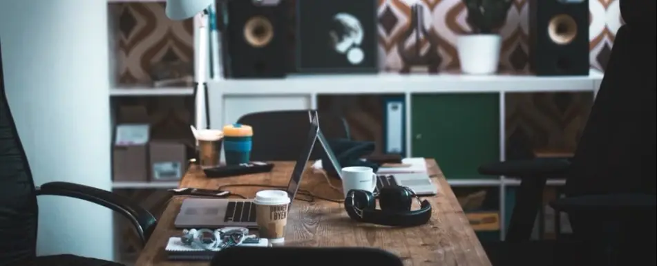 A work desk with two laptops, headphones and cups of coffee.