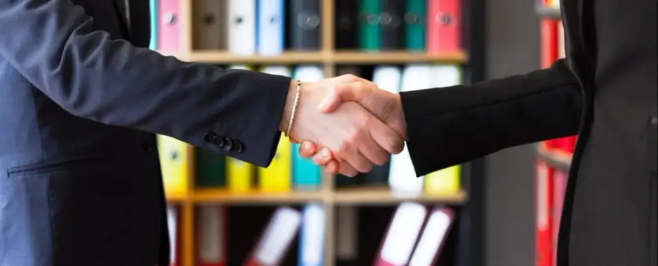 Two people shaking hands in a board room.