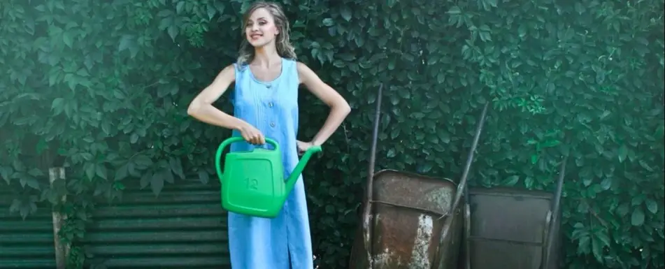 A woman in a garden with a green watering can.
