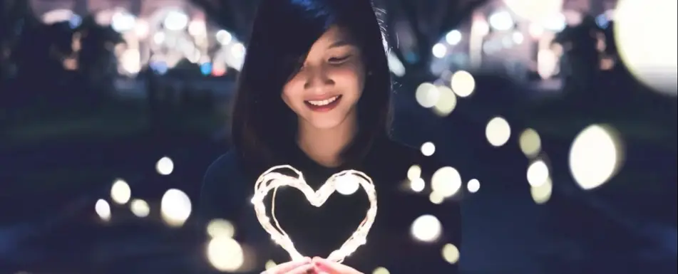 A person holding fairy lights in the shape of a heart.
