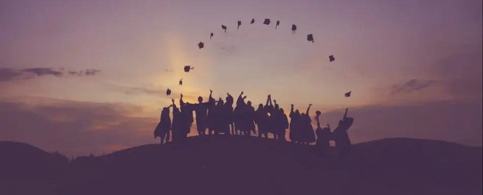 Graduates throwing their caps in the air with a sunset behind them.