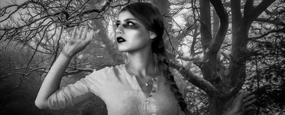 A woman wearing makeup poses dramatically in the woods.