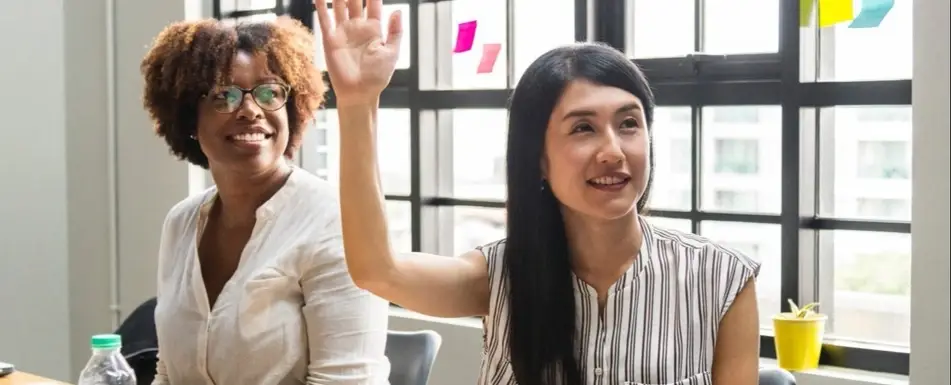 Two people at work. One of them is raising their hand.