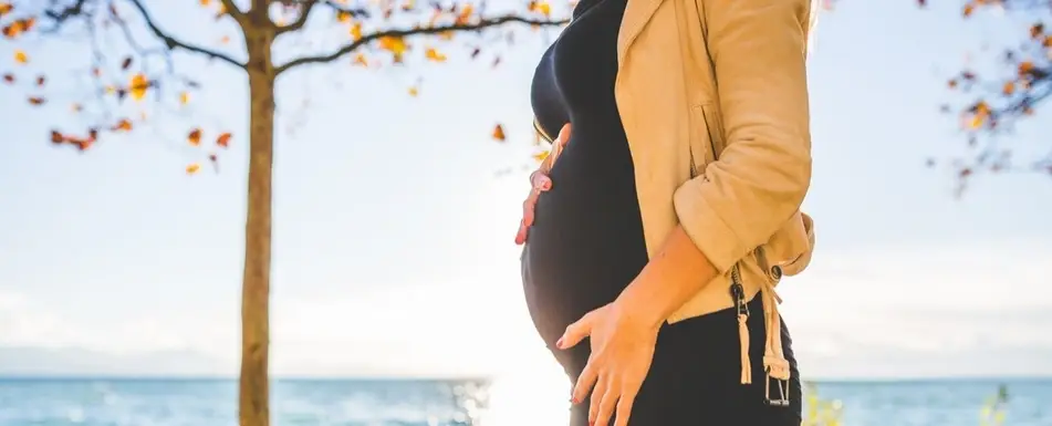A pregnant woman cups her belly while she walks.