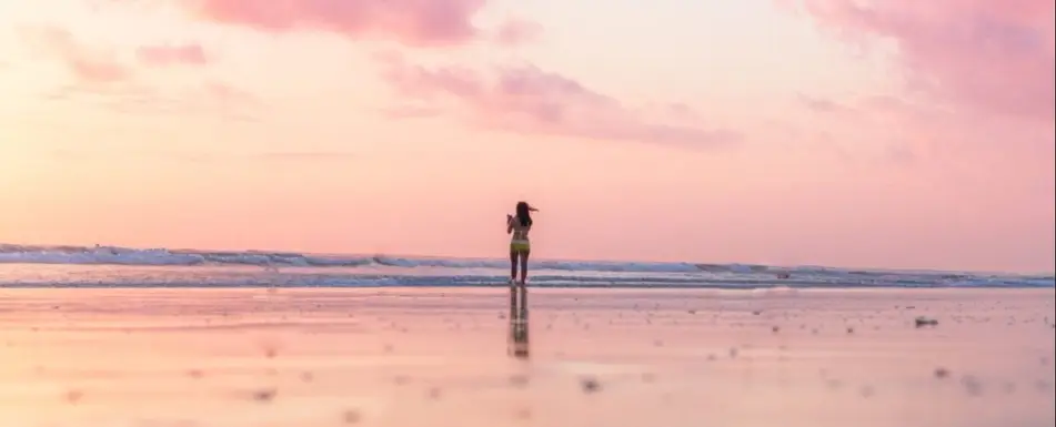 A person at the beach, standing by the edge of the water.