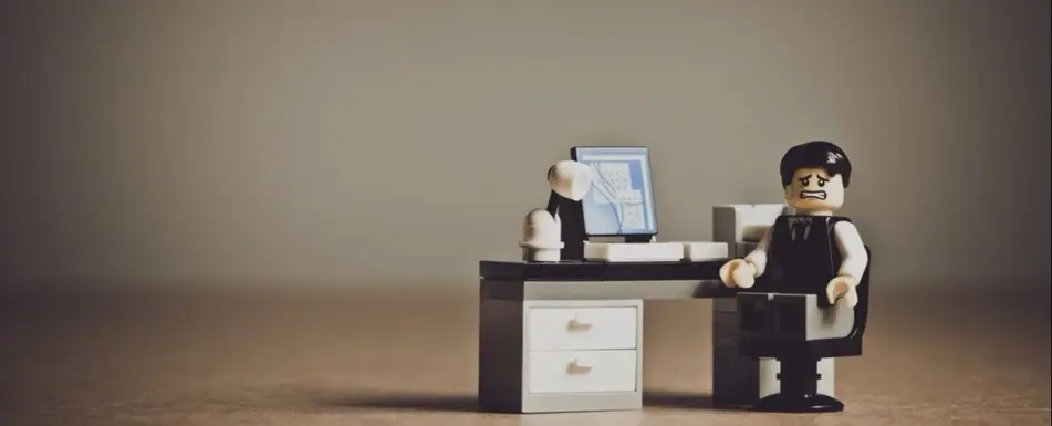 A lego of display of a human sitting by their work desk looking stressed.