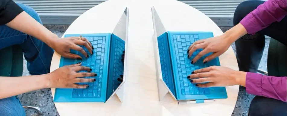Two people typing on laptops facing each other.