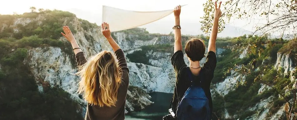 Two women stand triumphantly at the edge of a mountain.